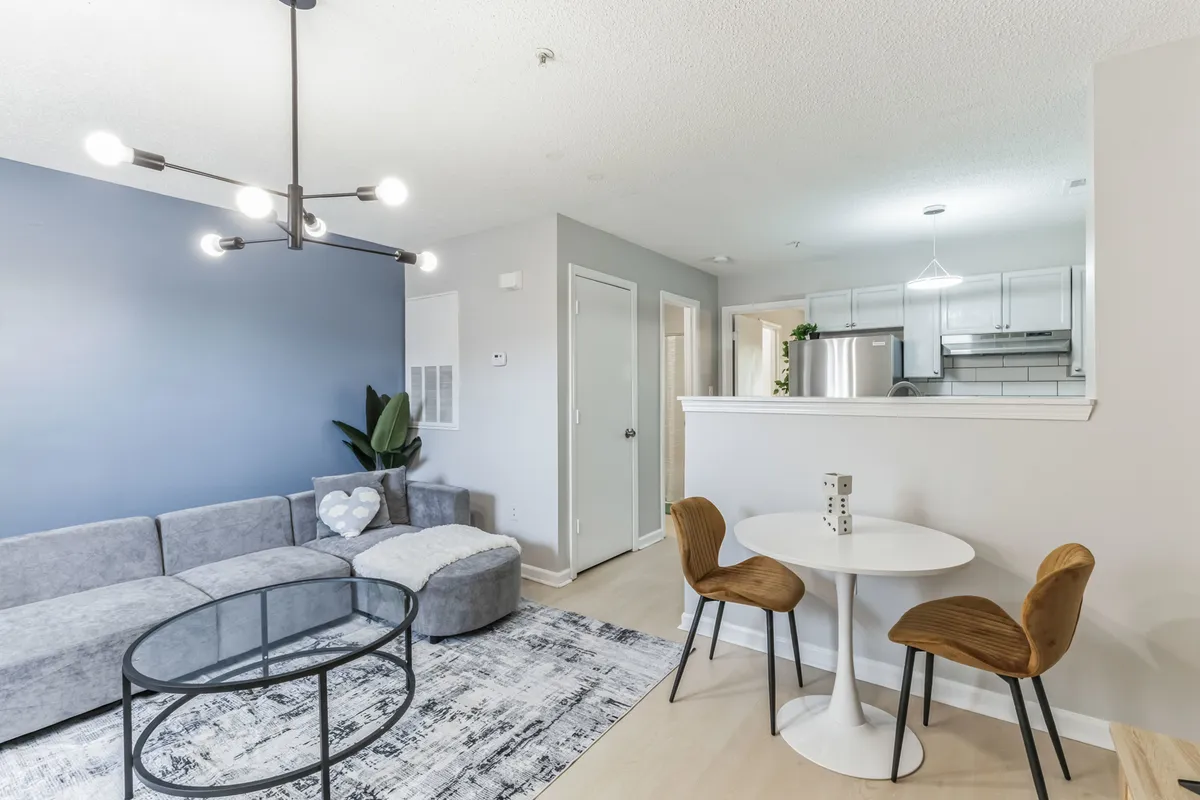 This inviting interior scene features a comfortable sofa, a stylish coffee table, and a dining table set for two, all arranged in a bright, open-concept living area. The space exudes warmth and is ideal for relaxing, sharing meals, or enjoying cozy evenings together.