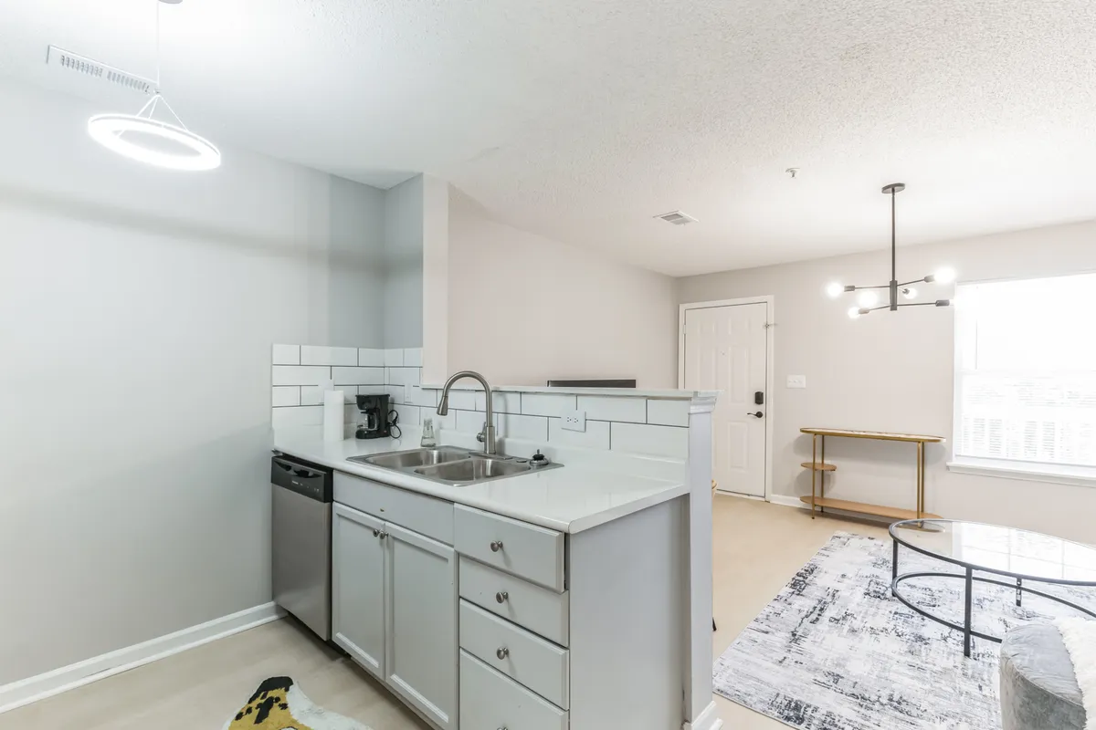 This image features a bright kitchen with a spacious countertop, a modern sink, stylish light fixtures, a dining table, and a cozy rug. The open-plan design allows for easy movement between the kitchen and dining area, creating an inviting space for cooking and entertaining.