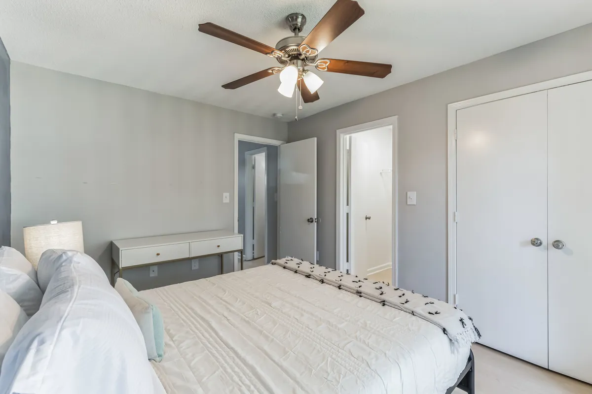 A beautifully arranged bedroom with a plush bed, modern ceiling fan, elegant light fixture, and a spacious dresser. The décor is inviting yet minimal, with subtle tones and ample storage, creating a restful environment ideal for relaxation and organization.
