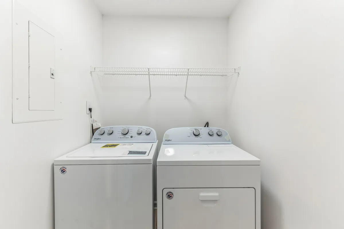 This image captures a neatly organized laundry area featuring a modern washing machine and dryer set beneath a practical shelf for supplies. The setting highlights everyday convenience and the comfort of handling laundry chores at home.