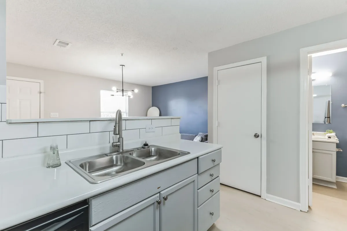 A well-lit kitchen space featuring a prominent kitchen sink, expansive countertop, modern light fixtures, and a striking blue accent wall. The setup is ideal for preparing meals, hosting family gatherings, or enjoying casual brunches.